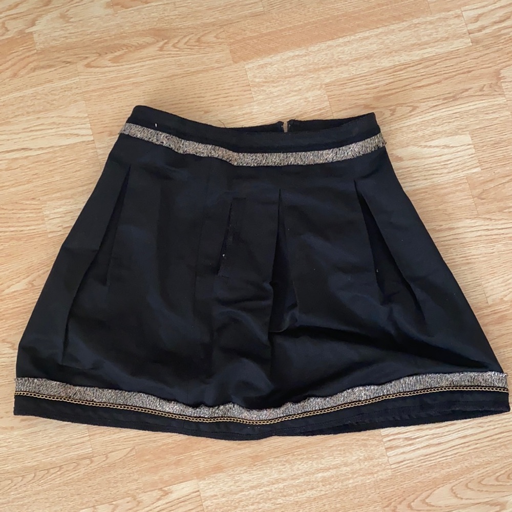 Black ruffle skirt with gold trim, has two pockets and a zipper in the back